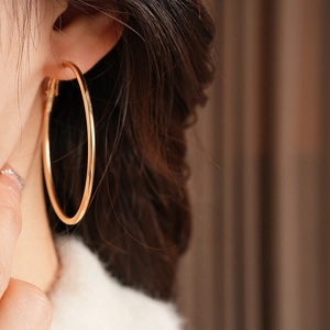 Close-up of vintage large gold metal hoop earrings worn by a model in warm light