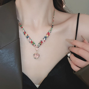 Close-up of a shimmering V-shaped necklace with colorful stones and a pink heart pendant