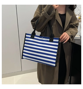 Dettaglio della borsa tote in tela a righe bianche e blu con robusti manici neri e bottone
