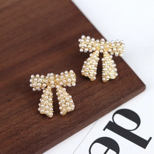 Elegant gold bow earrings with small white pearls on a minimalist wood background