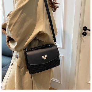 Close-up of black crossbody bag featuring V-shaped quilting and a metal butterfly buckle