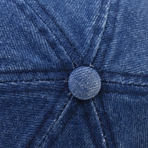 Macro shot of dark blue denim baseball cap top with stitched seams and metal button
