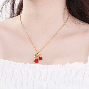 Close-up of a gold cherry pendant necklace with red rhinestones worn by a model