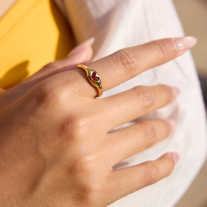 Detalle de anillo de sello dorado con dos piedras rojas en forma de corazón en la mano
