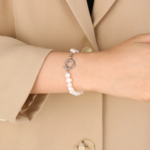 Détail d'un bracelet en perles avec fermoir OT en argent porté au poignet avec tenue chic