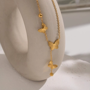 Elegant gold butterfly pendant necklace with metallic textures on a white circular stand