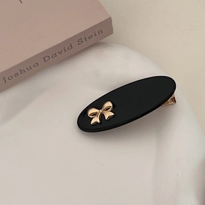 Detail of a chic black oval hair clip with a golden bow on a white decorative base