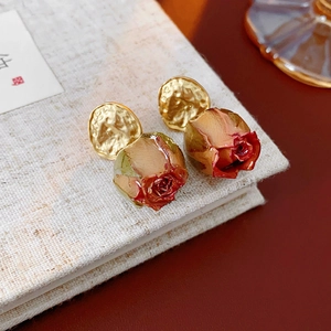 Macro shot of gold-plated red dried rose bud earrings resting on a vintage book
