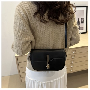 Detail of a black saddle bag with a golden vertical lock worn over a knit sweater