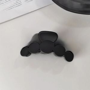 Vue détaillée de dessus d'une pince à cheveux noire mate au design minimaliste circulaire