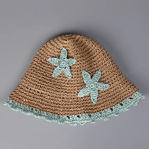 Close-up of handmade straw bucket hat with blue crochet star motifs and wavy edge detail