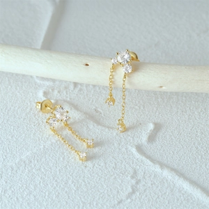 Detail shot of golden S925 silver tassel earrings with clear cubic zirconia on a wood branch