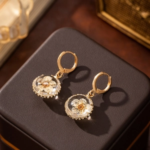 Detail of round glass ball earrings with dried flowers on a dark textured jewelry box