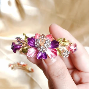 Macro shot of an enamel flower hair clip with purple and pink petals and rhinestones