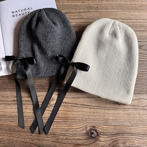 Set di berretti in maglia grigio e beige con fiocchi in raso nero su tavolo di legno
