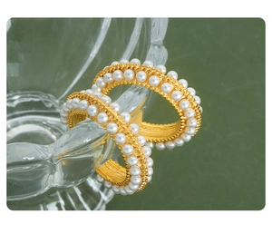 Macro shot of gold-plated hoop earrings with double-row faux pearl inlay on green backdrop