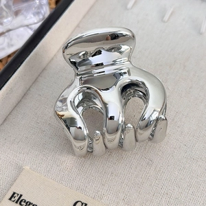 Close-up of heart-shaped silver metal hair claw clip with mirror finish on fabric tray