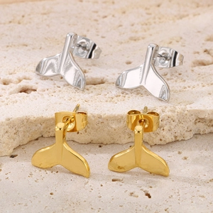 Macro detail of whale tail stud earrings in gold and silver finish on textured stone