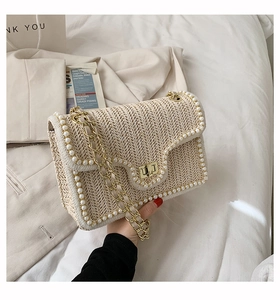 Detail of straw woven bag featuring white pearl trim and gold metal chain strap
