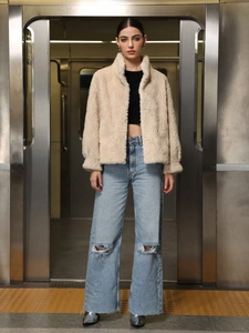 Damen Kunstpelzjacke in Beige mit Rippenstruktur über schwarzem Top und Jeans in der U-Bahn