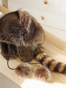 Close-up of raccoon style faux fur winter hat with striped tail and pom-poms