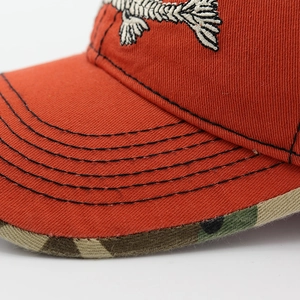 Close-up of fishbone embroidery and camouflage brim on orange canvas baseball cap