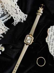 Détail de la montre carrée dorée avec lunette en cristal et chiffres romains sur fond vintage