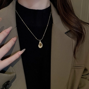 Detail of vintage teardrop necklace with dark gemstone and gold-tone bead chain on model