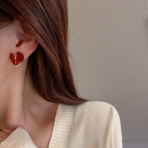 Close-up of red heart earrings with gold trim worn by a model in warm light