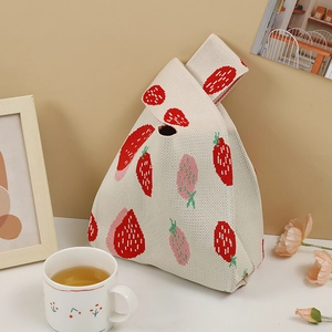 Detailed knit texture of a beige tote bag featuring red strawberry patterns and warm decor