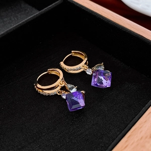 Detailed macro view of gold hoop earrings with small white zircons and purple crystal drop