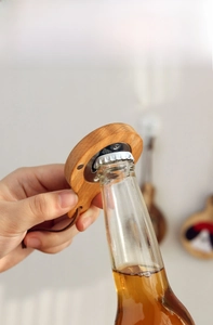 Gros plan d'une main utilisant le décapsuleur magnétique en bois sur une bouteille