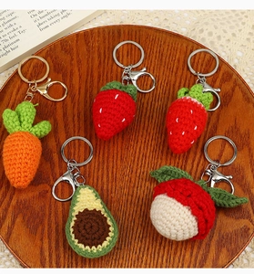 Close-up of handmade crochet fruit keychains including strawberry and avocado on wood tray