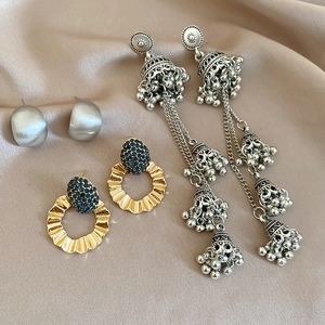 Macro shot of silver bow flower earrings and vintage jhumka tassels on silk