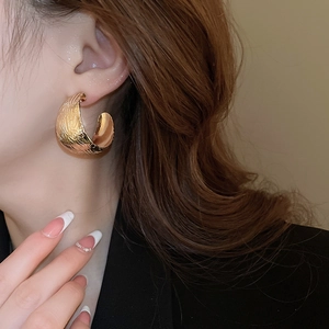 Vue détaillée de grandes boucles d'oreilles géométriques dorées en C avec finition texturée