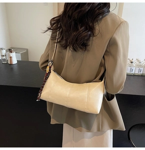 Detail of cream leather baguette bag with decorative pendant worn by a model in a suit