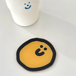 Close-up of a yellow cartoon smiley face coaster with black wavy edges on a white desk