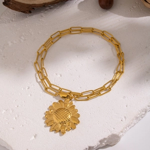 Macro detail of golden sunflower charm on a polished paperclip link chain bracelet