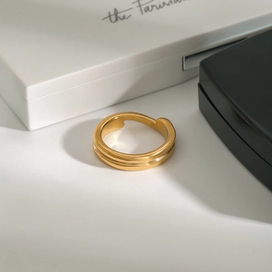 Vue macro d'une bague vague dorée à finition miroir sur emballage minimaliste chic