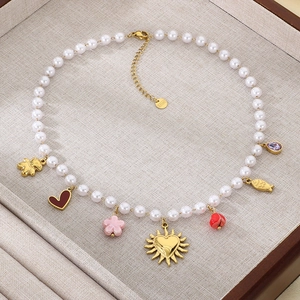 Detailed view of pearl necklace with gold fish, red hearts and floral charms on beige tray