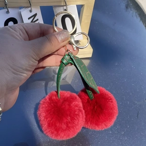 Close-up of fluffy cherry bag charm with red fur balls and golden metal clasp keychain