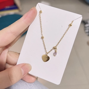 Detail of gold chain necklace featuring heart pendant and purple square bead charm