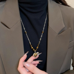 Close-up of a vintage flower pendant necklace with tiger eye stone on a model jacket