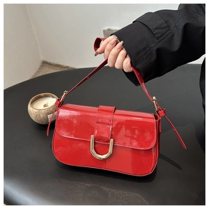 Detail of red patent leather handbag with golden horseshoe buckle held by a model