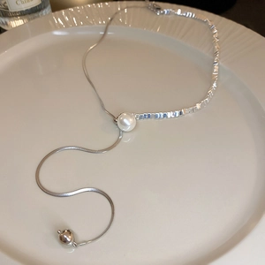 Detail of silver pearl fringe necklace on ceramic plate featuring sleek snake chain