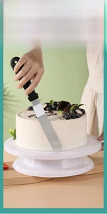 Detail of a food-grade PP cream spatula smoothing white cake on a rotating turntable