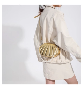 Detail einer goldenen muschelförmigen Umhängetasche mit eleganter weißer Perlenkette
