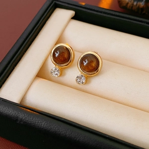 Elegante goldene Ohrringe mit braunen Kunststeinen und klaren Strasssteinen auf Polster