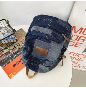 Detail of dark blue denim backpack with white stitching and brown leather zipper pull