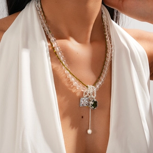 Close-up of layered necklace featuring crystal pendant, green stones, and pearl drop detail
